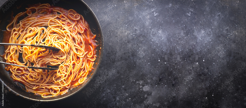 Tomato pasta is cooked in a frying pan on the kitchen banner background. Italian pasta banner background. Italian food and cuisine concept. Tomato pasta is cooked in a frying pan on the kitchen banner background. Italian pasta banner background. Italian food and cuisine concept.