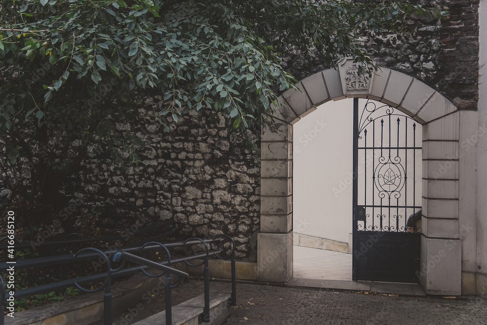 Obraz premium The entrance to a Monastery foundation Paulinow na Skalka in the Christian part of Kazimierz district in Krakow, closed by a rusty metal grating in arch. Iron arched gate in an old stone wall with ivy