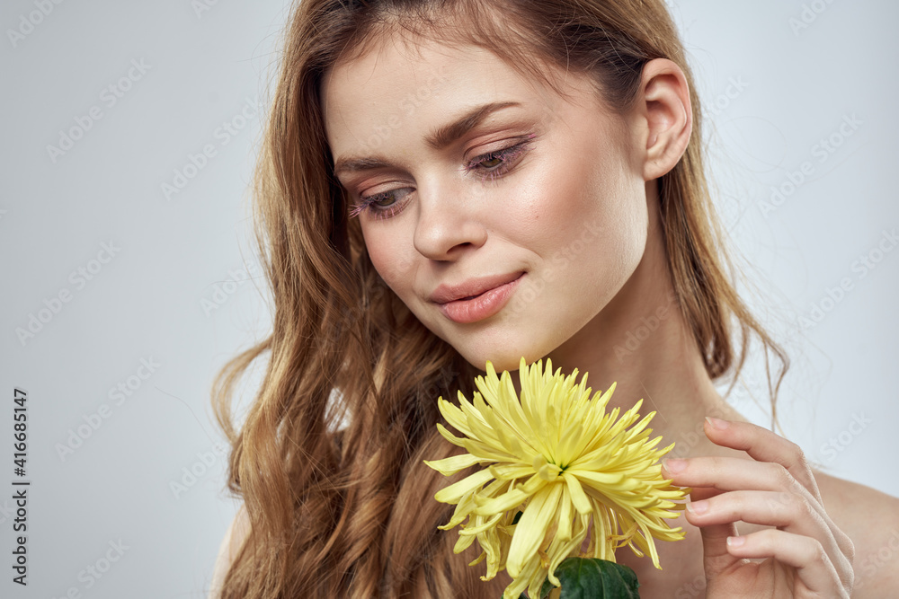 Portrait of a beautiful woman with a yellow flower on a light background charming smile model red hair Portrait of a beautiful woman with a yellow flower on a light background charming smile model red hair