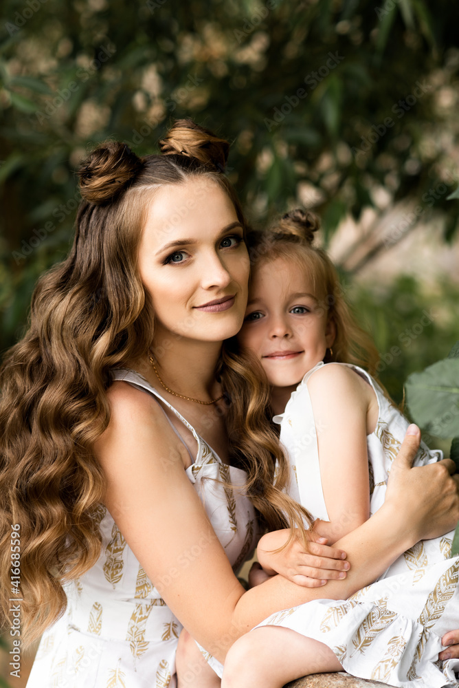 Happy woman mom plays with her daughter outside in matching dresses on a sunny day