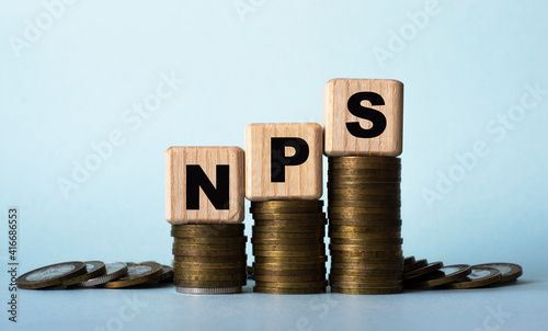 NPS - acronym on wooden cubes. Which stand on stacks of coins on a light background