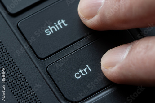 Fingers holding down Shift and Ctrl keys together on a black laptop computer.