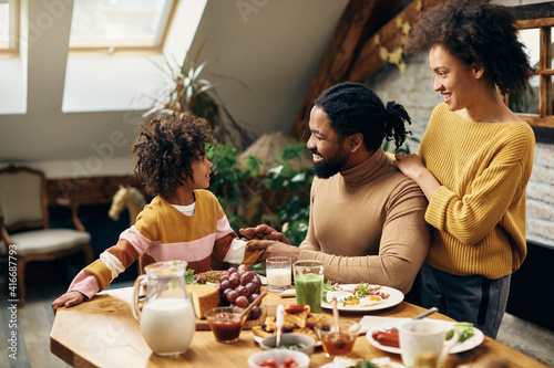 Happy African American parents talking to their daughter at dining table.