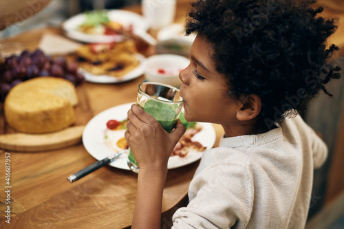 Small African American boy drinking smoothie during breakfast.
