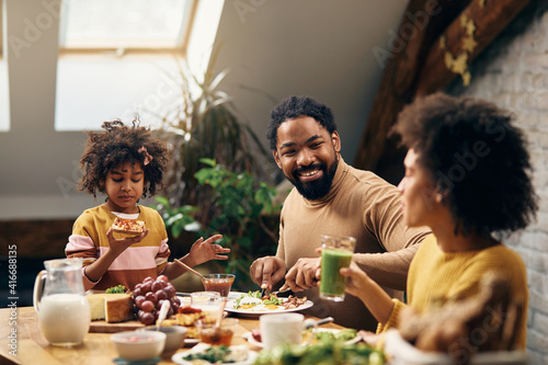 Happy black family talking while having breakfast at home.