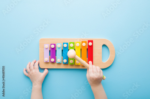 Baby hand holding hammer and playing colorful xylophone on light blue table background. Closeup. Music toy instrument of development for little kids. Point of view shot. Top down view. photo