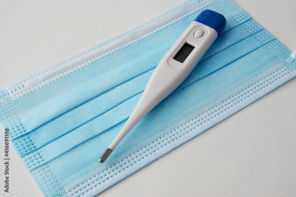 Medical mask and electronic thermometer on white background Medical mask and electronic thermometer on white background