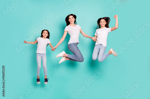 Full length body size photo sisters jumping up wearing jeans white t-shirts happy won lottery isolated bright blue color background