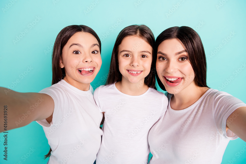 Photo portrait of sisters smiling happy taking selfie showing tongue fooling childish playful isolated vibrant blue color background