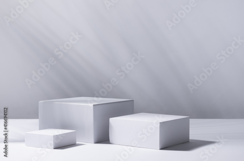 White square podiums in sunlight with shadow palm leaf in white space. Tropical showcase for cosmetic products, goods, shoes, bags, watches.