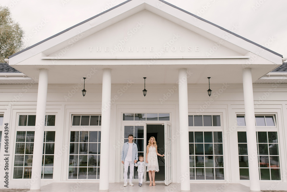 Fototapeta premium Beautiful young family man woman and son in smart clothes on the background of a luxurious white house