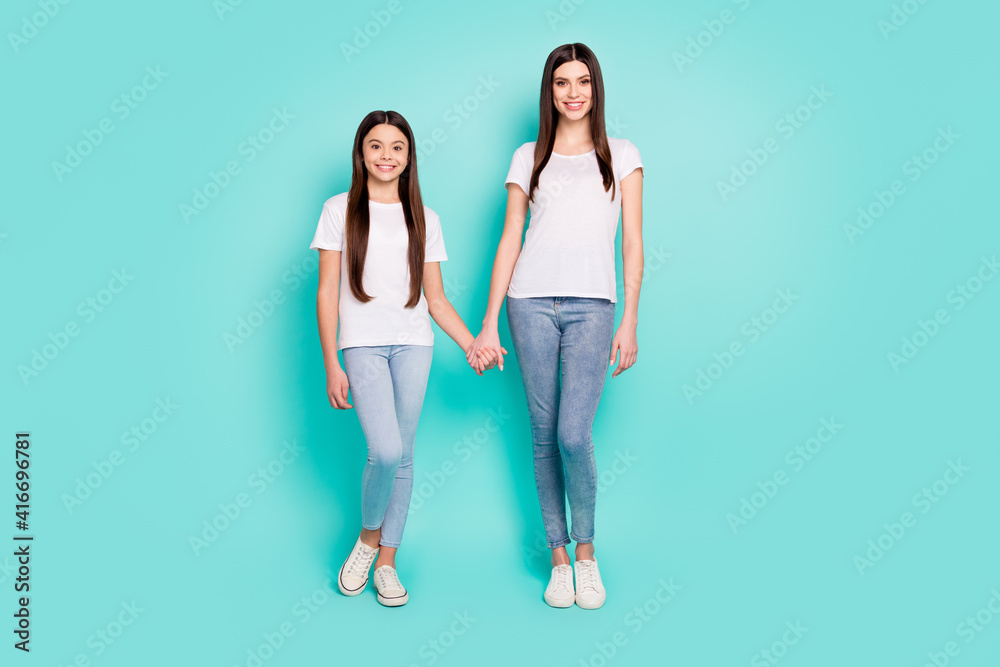 Obraz premium Full length body size photo of two cheerful sisters holding hands isolated on bright blue color background