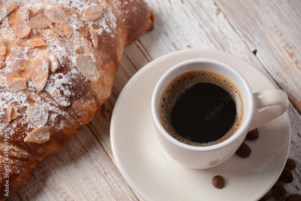 Fresh croissant with a cup of coffee, roasted beans on vintage background