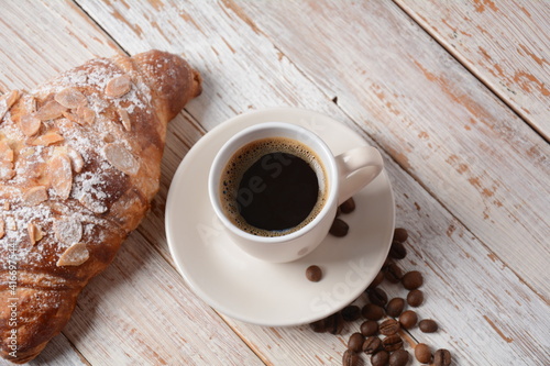 Fresh croissant with a cup of coffee, roasted beans on vintage background