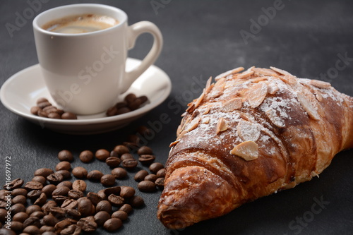 Fresh croissant with a cup of coffee, roasted beans on vintage background