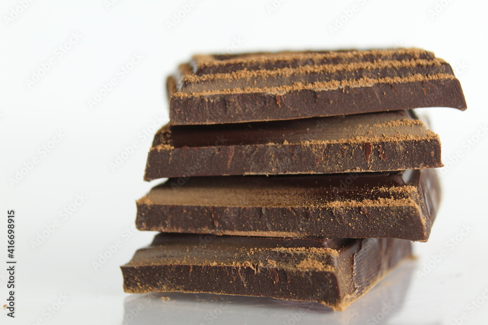 Dark bitter chocolate pieces stacked slide lies on a white background with a reflection with a place for text and copyspace Dark bitter chocolate pieces stacked slide lies on a white background with a reflection with a place for text and copyspace