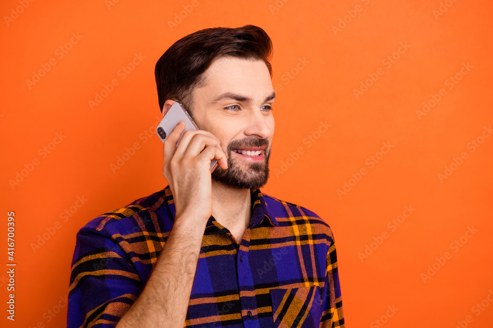 Portrait of cheerful person speak phone beaming smile wear checkered outfit isolated on orange color background