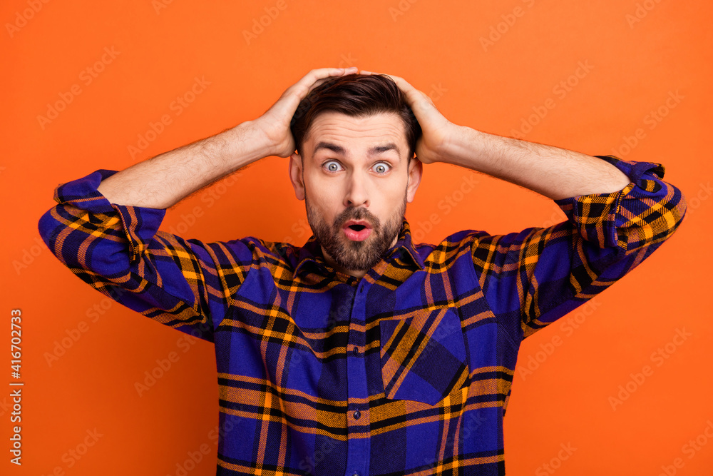Photo of young guy hands touch head amazed shocked surprised fake novelty news isolated over orange color background Photo of young guy hands touch head amazed shocked surprised fake novelty news isolated over orange color background