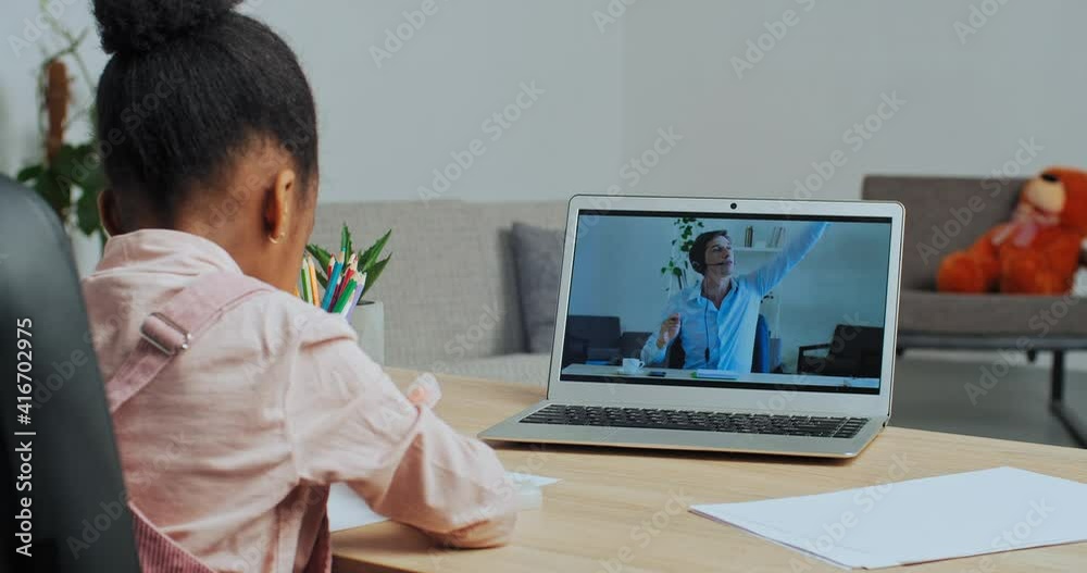Afro american little schoolgirl ethnic child engaged with internet teacher makes video call from home learns to draw picture with online tutor repeats after man on laptop screen, education in lockdown