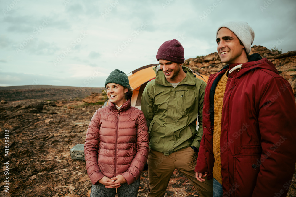 Smiling group of caucasian friends camping on top of mountain with tent