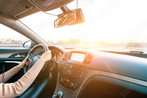 Business woman driving car. Travel car trip on road at sunset. Happy young woman have fun ride inside vehicle in winter sunny day.