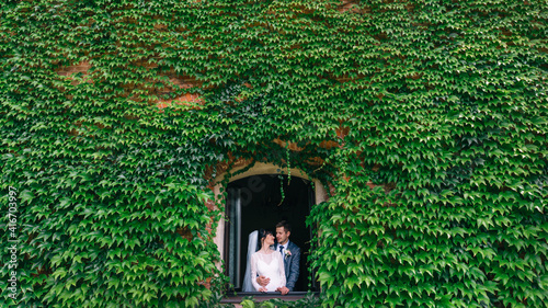 stylish bride and groom on their wedding day hug and smile while walking in the building in the window with walls and ivy. photo