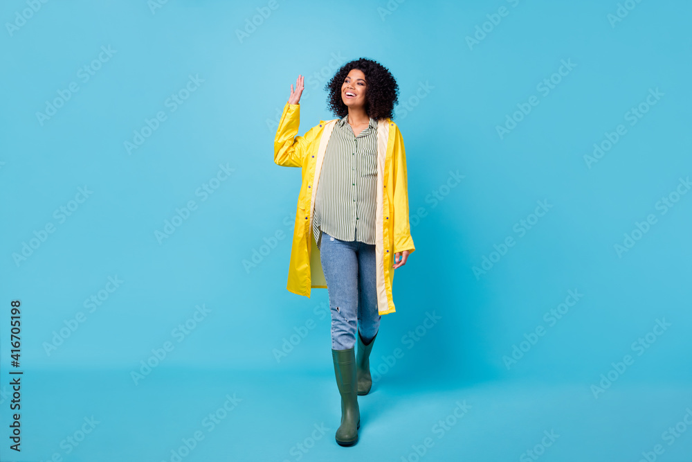 Photo of adorable charming dark skin lady wear yellow overcoat walking waving arm isolated blue color background Photo of adorable charming dark skin lady wear yellow overcoat walking waving arm isolated blue color background