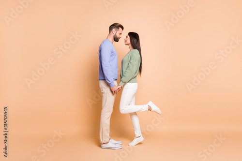 Full length body size profile side view of nice amorous couple soulmates meet holding hands isolated on beige pastel color background
