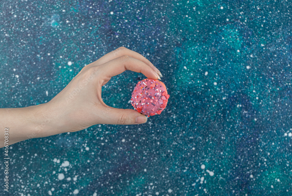 Female hand holding pink cookie with sprinkles Female hand holding pink cookie with sprinkles