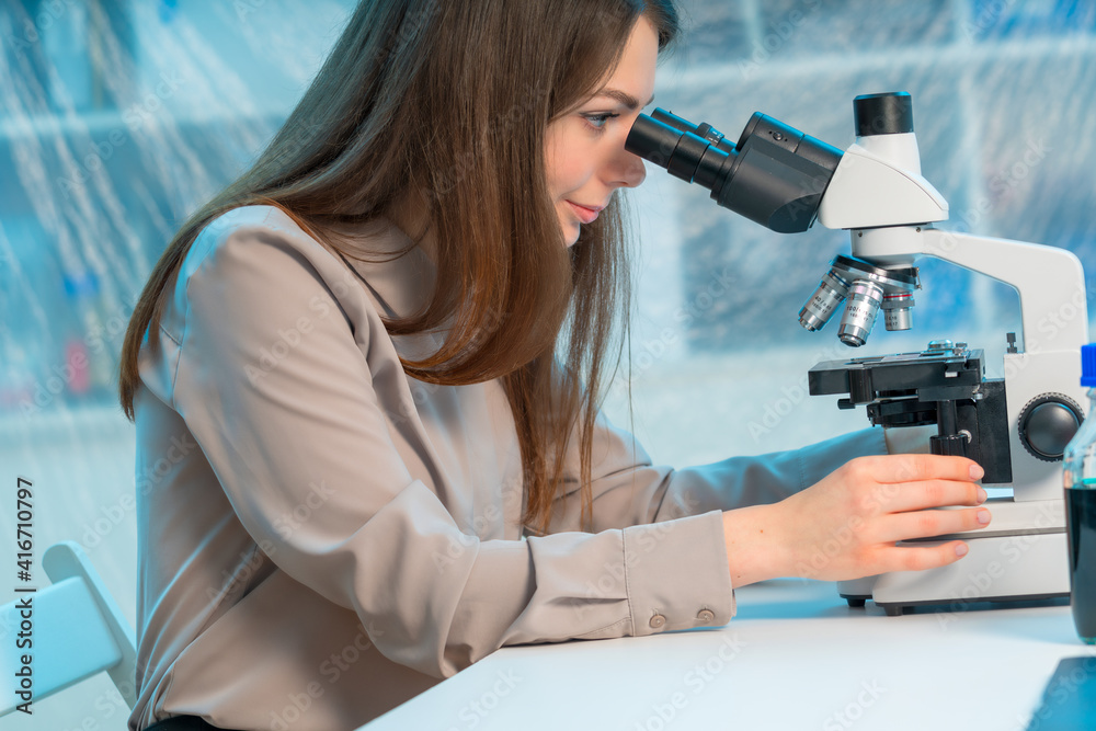 Fototapeta premium Young woman student working on a microscope while sitting at the table