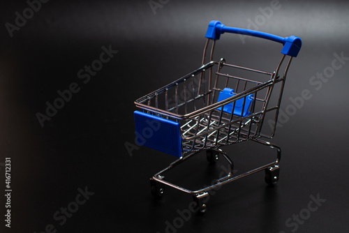 Small blue shopping cart on a black background. Copspace