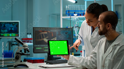 Professional chemists working on tablet with green screen mock up and testing virus evolution, developing vaccine, drugs and antibiotics standing in high tech laboratory with chroma key display