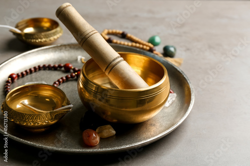 Composition with golden singing bowl and mallet on grey table, closeup. Sound healing