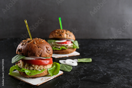 Vegetarian hamburger with tomato, lettuce, onion, bean cutlet and grain bun on dark  background. It  is an alternative to the usual hamburger.  The concept of healthy eating. Copy space.