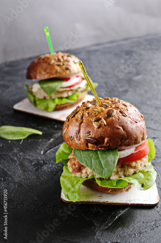 Vegetarian hamburger with tomato, lettuce, onion, bean cutlet and grain bun on dark  background. It  is an alternative to the usual hamburger.  The concept of healthy eating. Vertical.