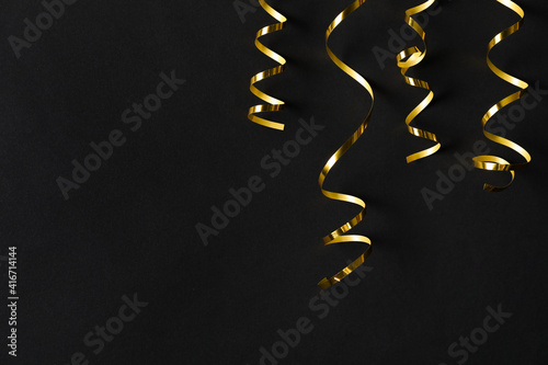 Shiny golden serpentine streamers on black background, flat lay. Space for text