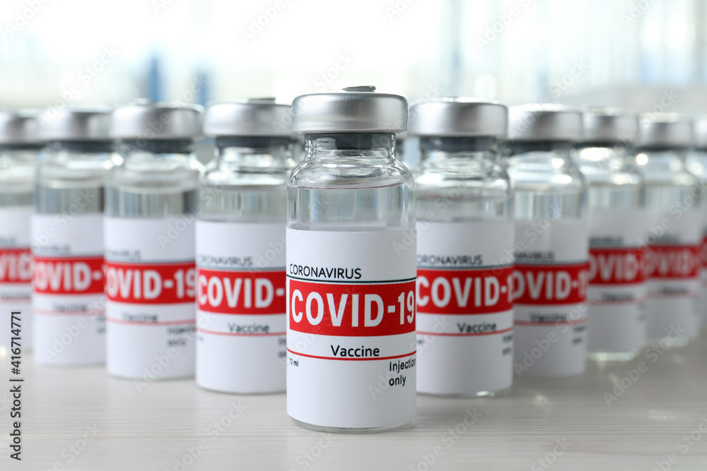 Glass vials with COVID-19 vaccine on white wooden table