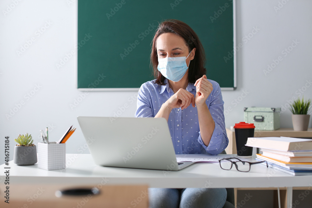 Teacher with protective mask conducting online lesson in classroom during COVID-19 quarantine Teacher with protective mask conducting online lesson in classroom during COVID-19 quarantine