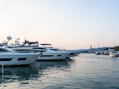 The yachts are moored in the calm sea and the silhouette of the mountains can be seen in the distance