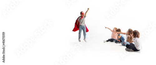 Flyer. Child pretending to be a superhero with her friends sitting around her. Kids excited, inspired by their strong, brave friend in red coat isolated on white background. Dreams, emotions concept.