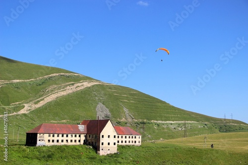 hang glider and a house with a red roof in the morning in the mountains. hang glider in the mountains. blue sky  house with red tiles  Caucasus mountains.