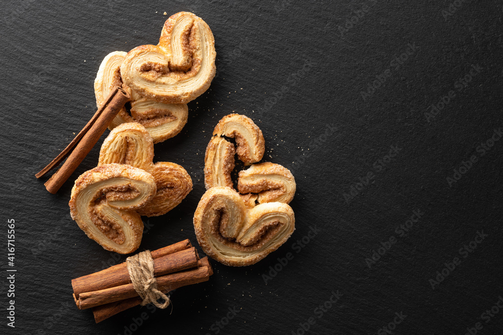 crispy puff pastry with sugar and cinnamon on a black stone background, top view, place for text crispy puff pastry with sugar and cinnamon on a black stone background, top view, place for text