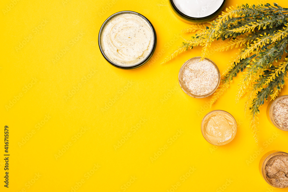Cosmetic containers with skincare products on illuminating yellow background. Natural body scrub and moisturizing face cream or skin clay mask. Flat lay composition, copy space Cosmetic containers with skincare products on illuminating yellow background. Natural body scrub and moisturizing face cream or skin clay mask. Flat lay composition, copy space