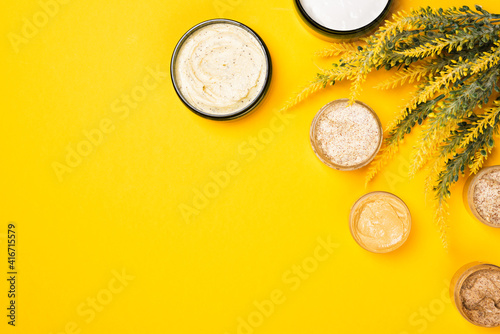 Cosmetic containers with skincare products on illuminating yellow background. Natural body scrub and moisturizing face cream or skin clay mask. Flat lay composition, copy space