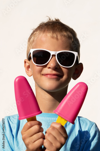 Portrait of a beautiful blonde teenager in white sunglasses holding two bright cold ice cream cones on a summer day