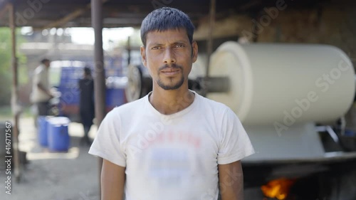 outdoor close up shot of a Indian male local textile mill labourer standing and looking at camera on a broad daylight photo