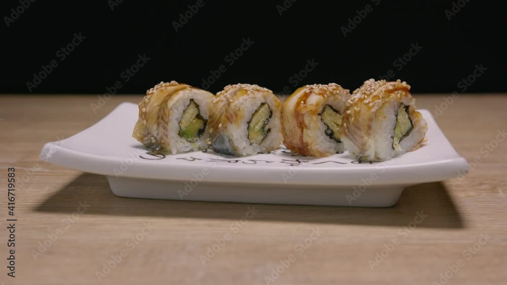 Stylized Japanese plate with sushi roll set sliding over wooden table. Close up Stylized Japanese plate with sushi roll set sliding over wooden table. Close up