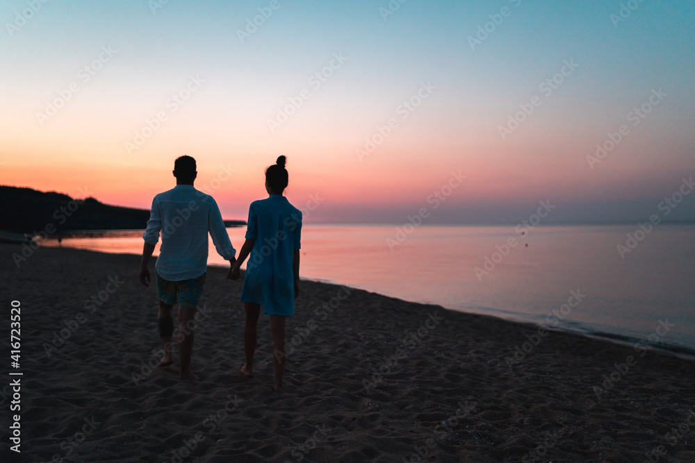 Silhouette of european couple holding each other hands and walking on the beach during sunset