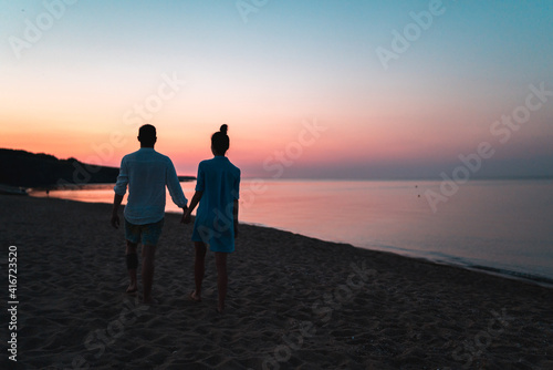 Silhouette of european couple holding each other hands and walking on the beach during sunset