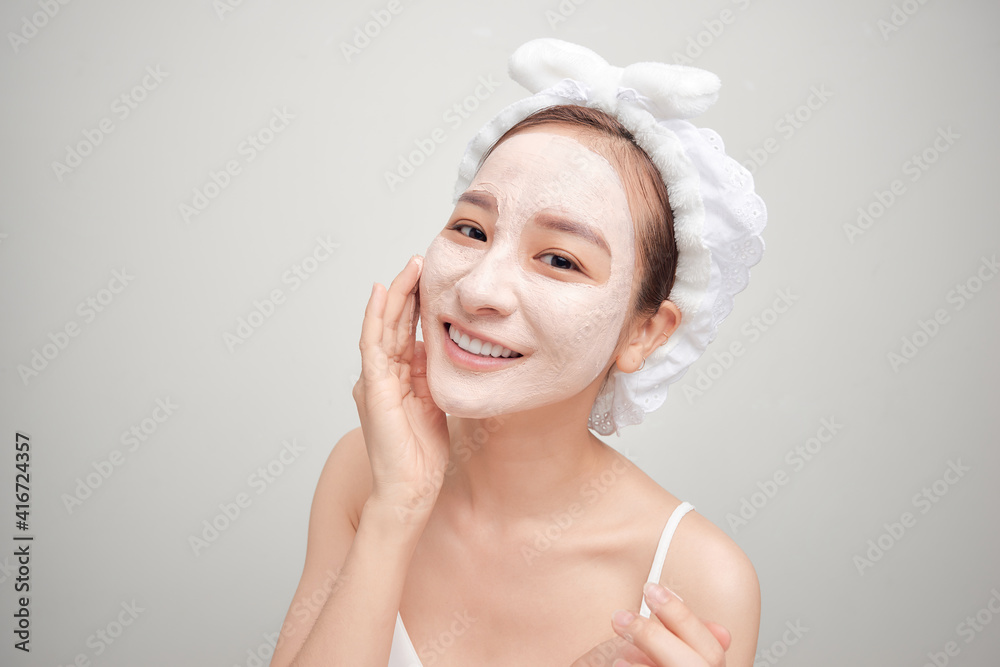 Young Asian woman applying facial clay mask over white background. Beauty treatments concept.